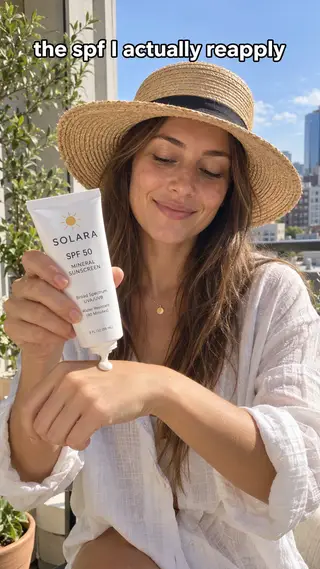 Anuncio UGC de TikTok de una mujer con sombrero de paja echándose protector solar mineral en la mano en la playa