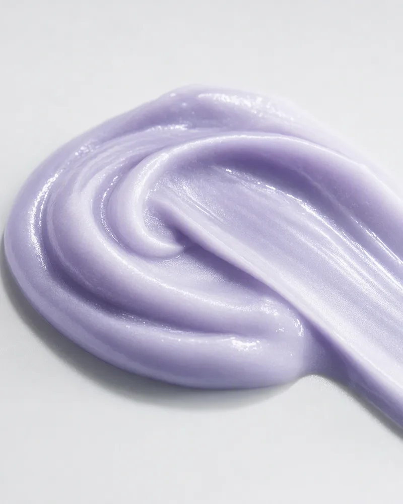 Texture swatch of a lilac eye serum cream, swirled on a light grey background