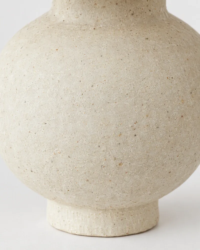 Side view of the cream stoneware vase showing its round body and small foot
