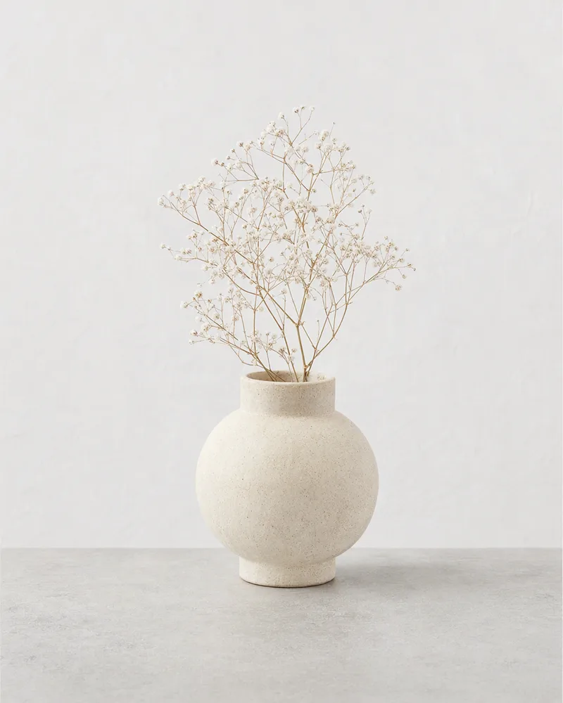 The cream ceramic vase with a few dried gypsophila stems on a pale stone surface