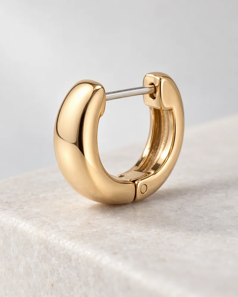 Close-up of a single gold huggie hoop with its hinged closure open