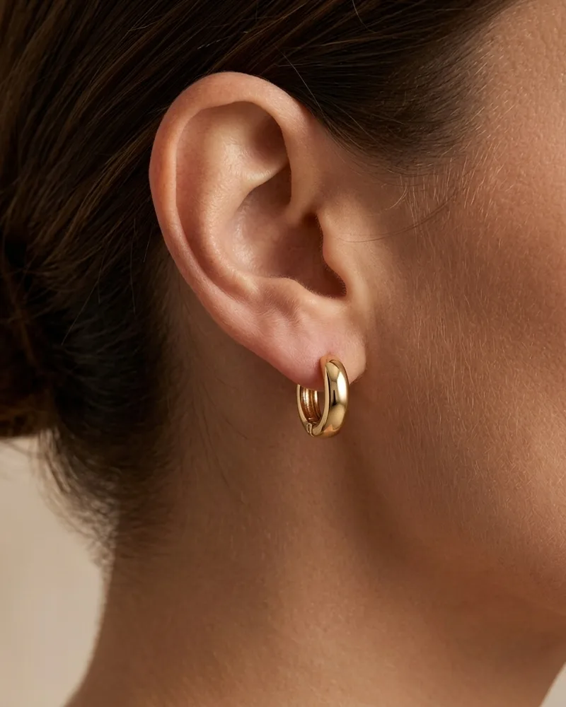 Close-up of a woman's ear wearing a small gold huggie hoop earring