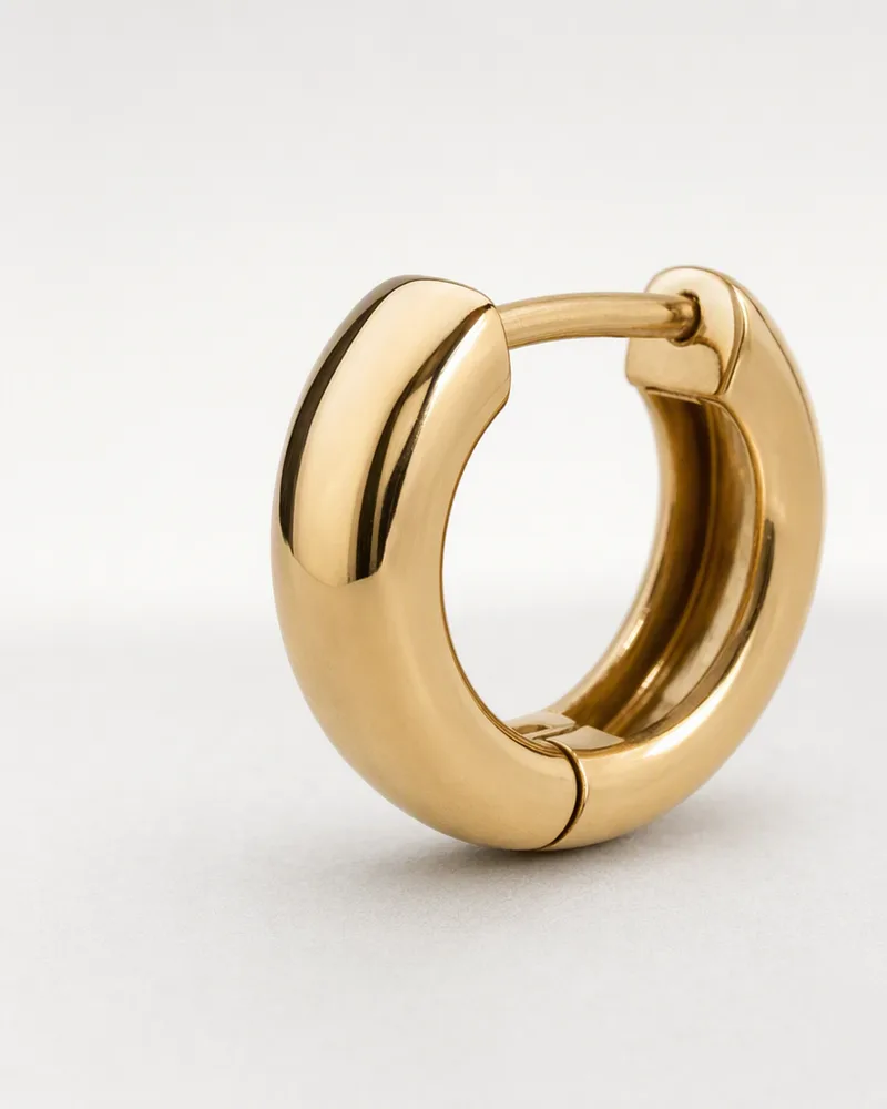 A single gold huggie hoop seen from the side, showing its thickness