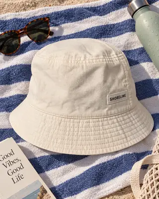 Sombrero de pescador Shoreline sobre una toalla de playa con gafas de sol, un libro y una botella de agua
