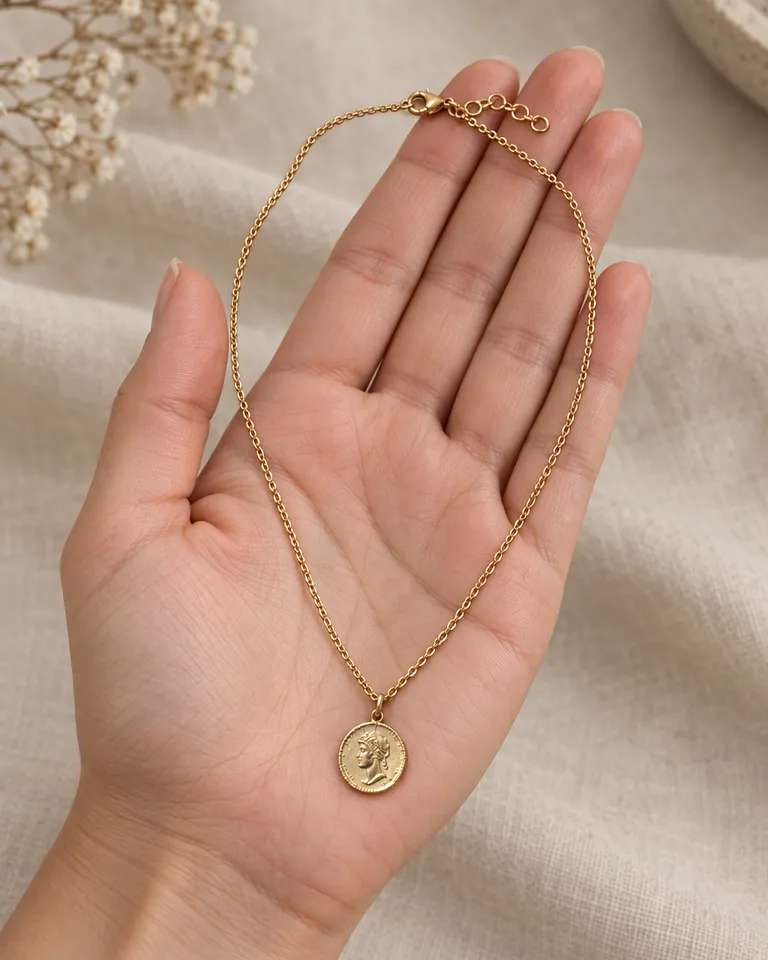 Collar de moneda dorado sobre la palma abierta de una mano para mostrar el tamaño del colgante