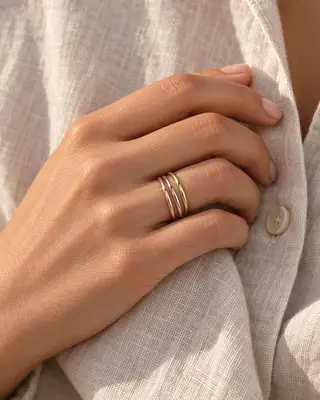 Mano de una mujer con los tres anillos apilables sobre una camisa de lino con luz cálida